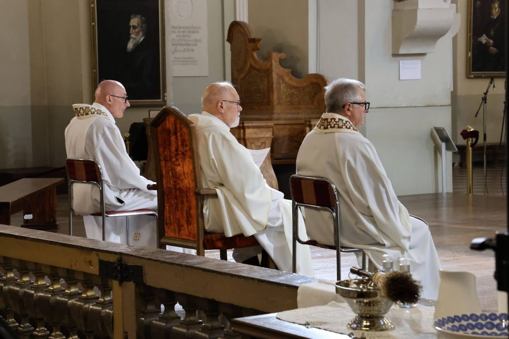 Trys kunigai sėdi ant kėdžių